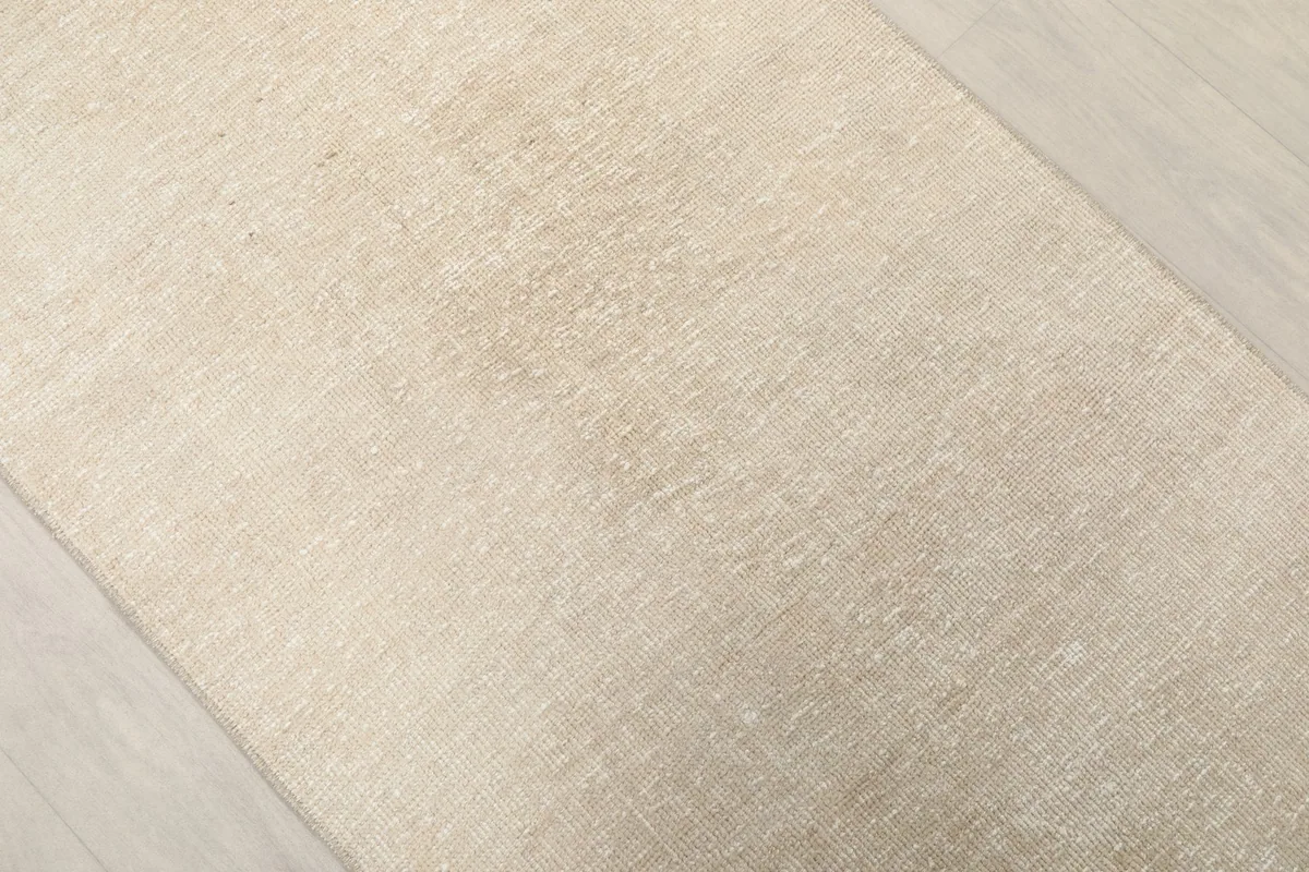 Oblique view of the vintage beige runner, showcasing its soft hue and worn texture.