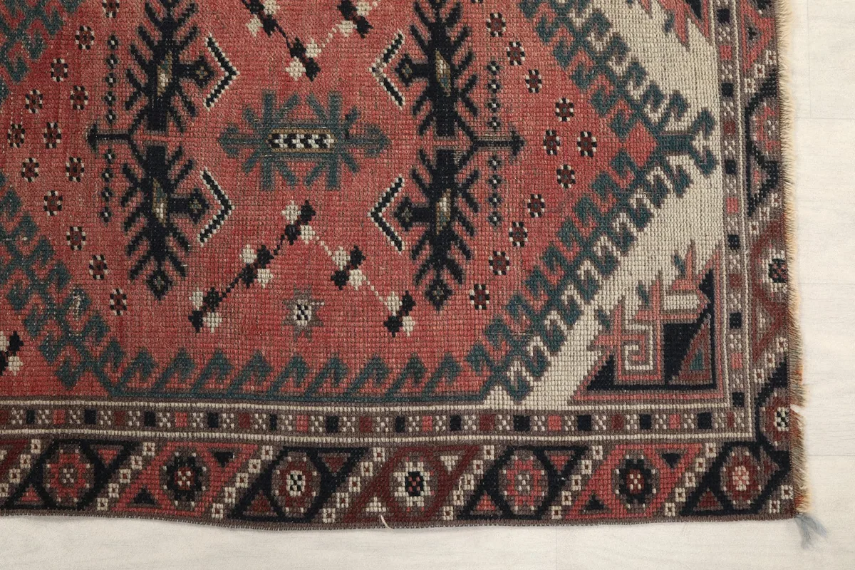 Detailed view of the rug's corner, showcasing the rust field, black and gray geometric patterns, and cream accents.
