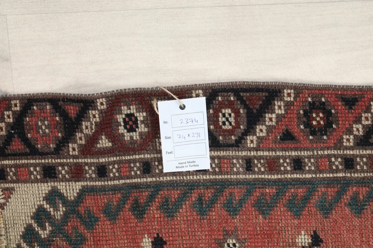 Close-up of the rug's edge with a size tag displaying the dimensions 2'5" x 9'7" (74 x 291 cm).