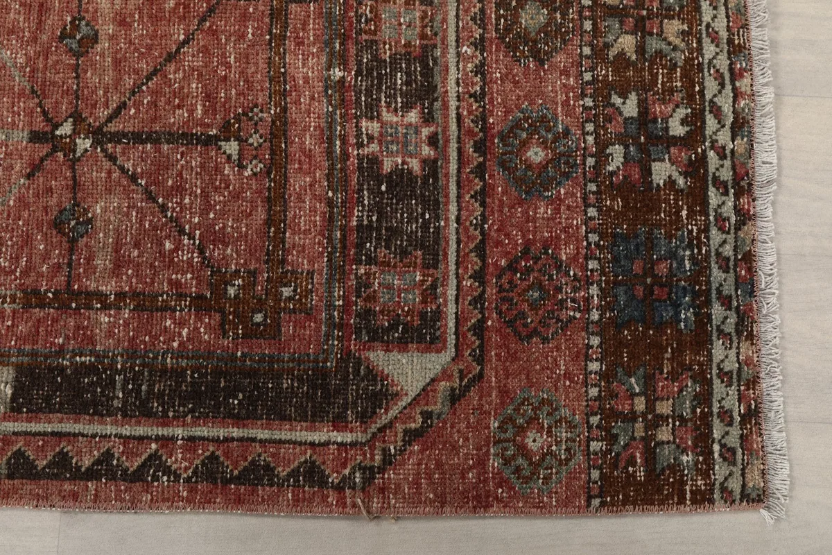 Detailed view of one end of the rust runner rug, showing the intricate tribal motifs and border.