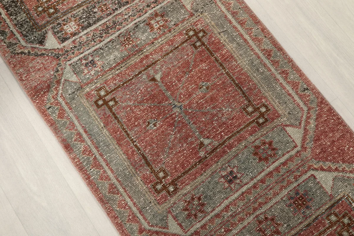 Close-up of a central geometric panel on the runner rug, with rust and gray colors and visible wear.