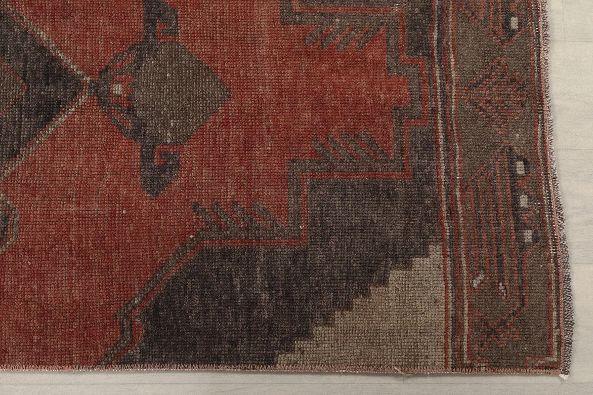 Detailed view of the rug's corner, showing the rust field and charcoal geometric border design.