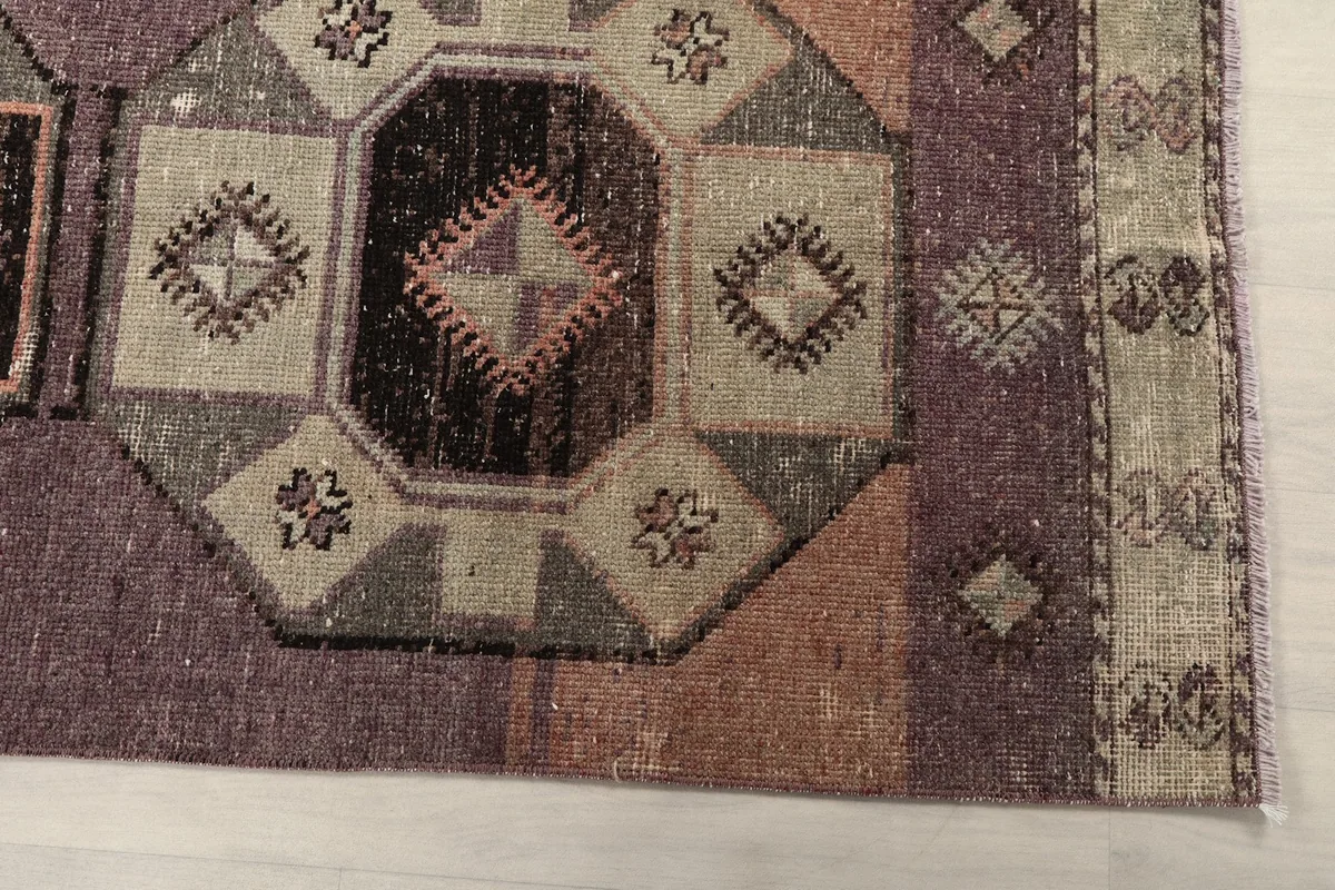 Detailed view of the purple field and geometric border pattern at one end of the rug