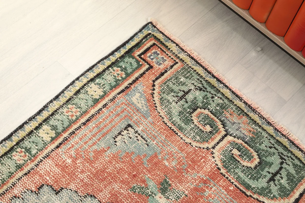Detailed view of the rug's border pattern and corner design in green and rust