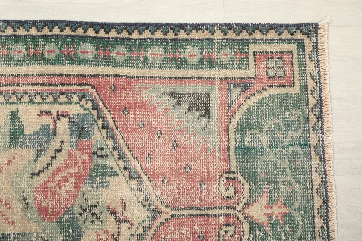 Corner detail of the rug showing the green border and faded rose field with motifs.