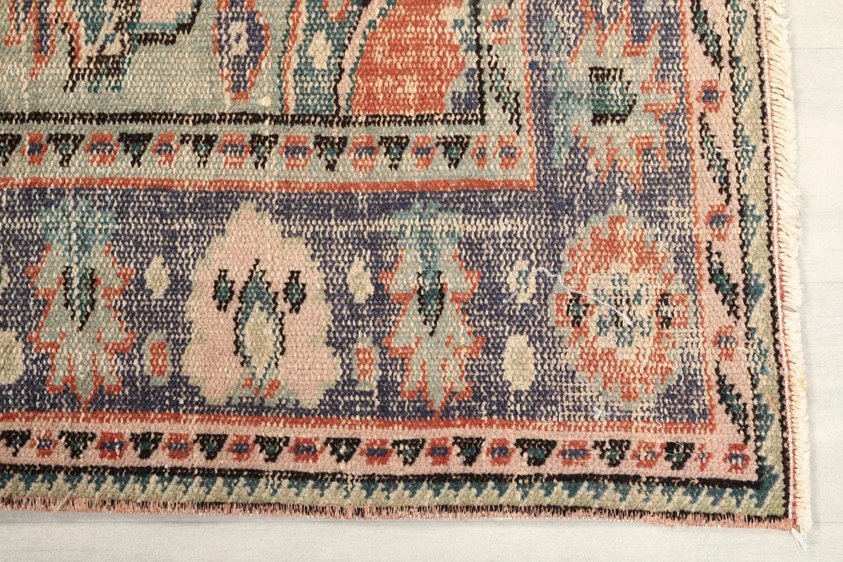 Detail of the blue border and corner motif with beige and pink accents on the rug