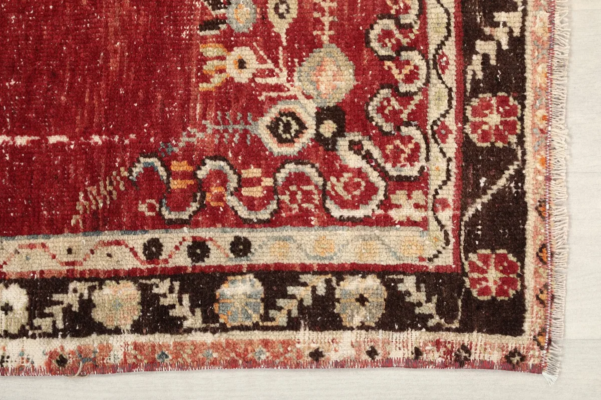 Detailed view of the rug's lower right corner showing the geometric border and distressed red field