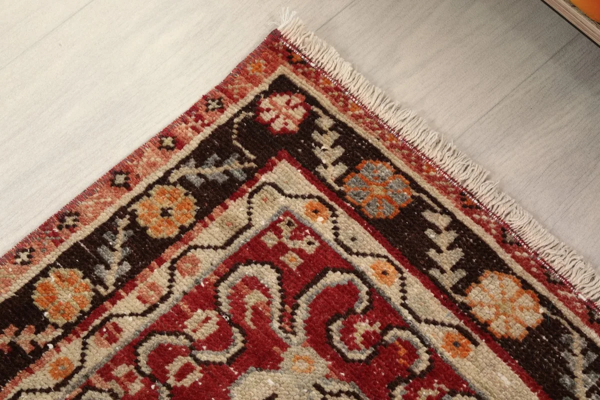 Close-up of the upper left corner of the rug, showing the brown and ivory border with floral designs