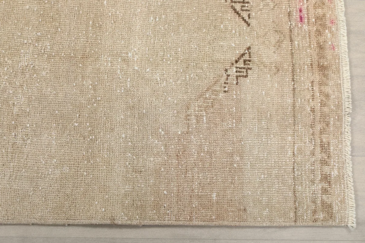 Detailed view of the rug's beige and ivory field, showing distressed wool pile and a hint of rose color