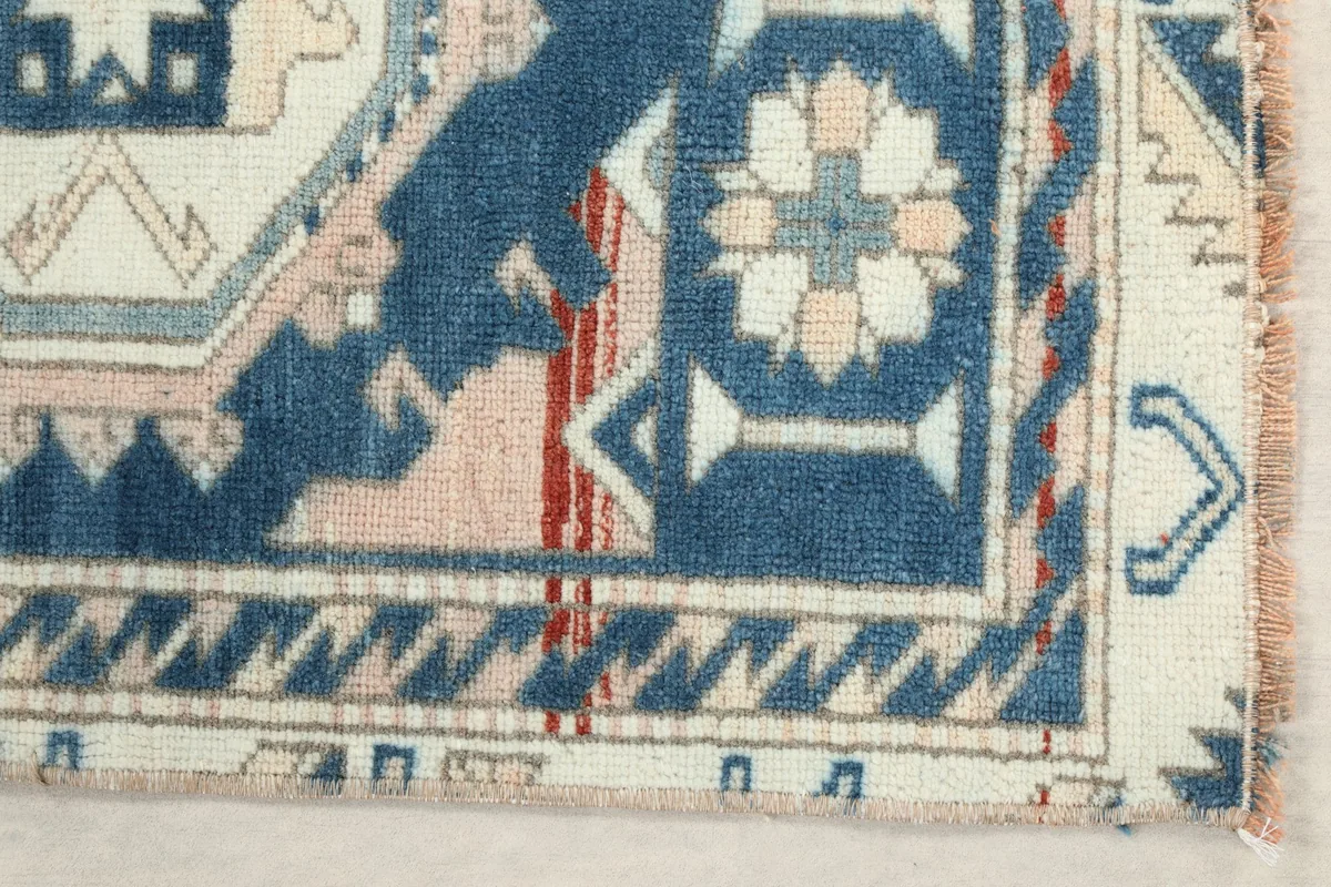Detail of the rug's corner, showing the blue border with geometric motifs and a subtle red accent