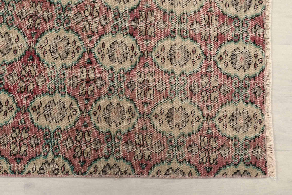 Detailed view of the repeating geometric motifs in rose, beige, and blue, showing the rug's texture.
