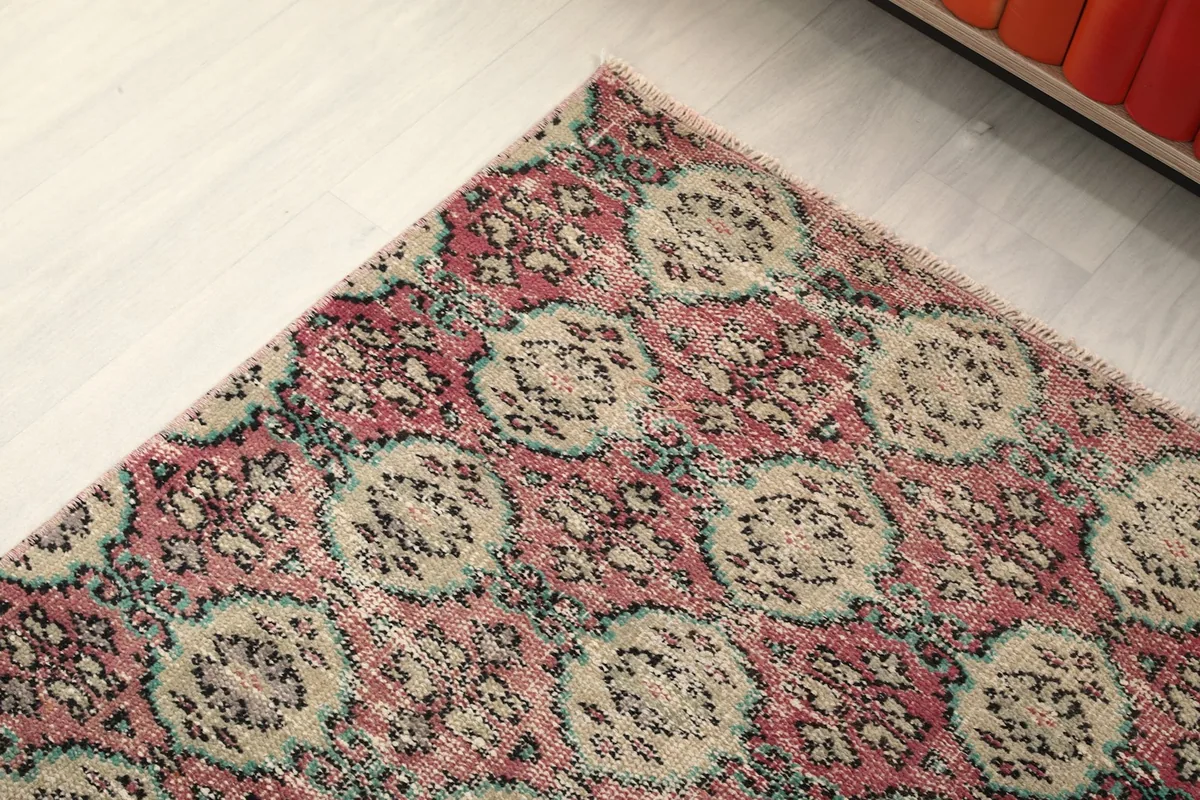 Corner detail of the vintage runner rug, showcasing the faded rose field and beige geometric patterns.