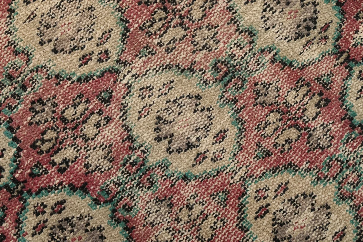 Extreme close-up of the low wool pile, showing the hand-knotted texture and color variations in the rose, beige, and blue.