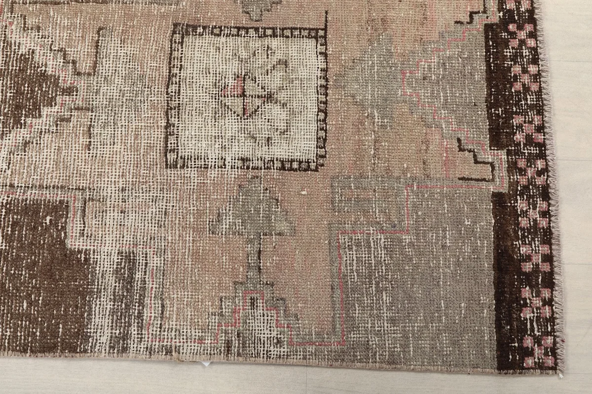 Detailed view of the rug showing its distressed beige, brown, and pink geometric motifs
