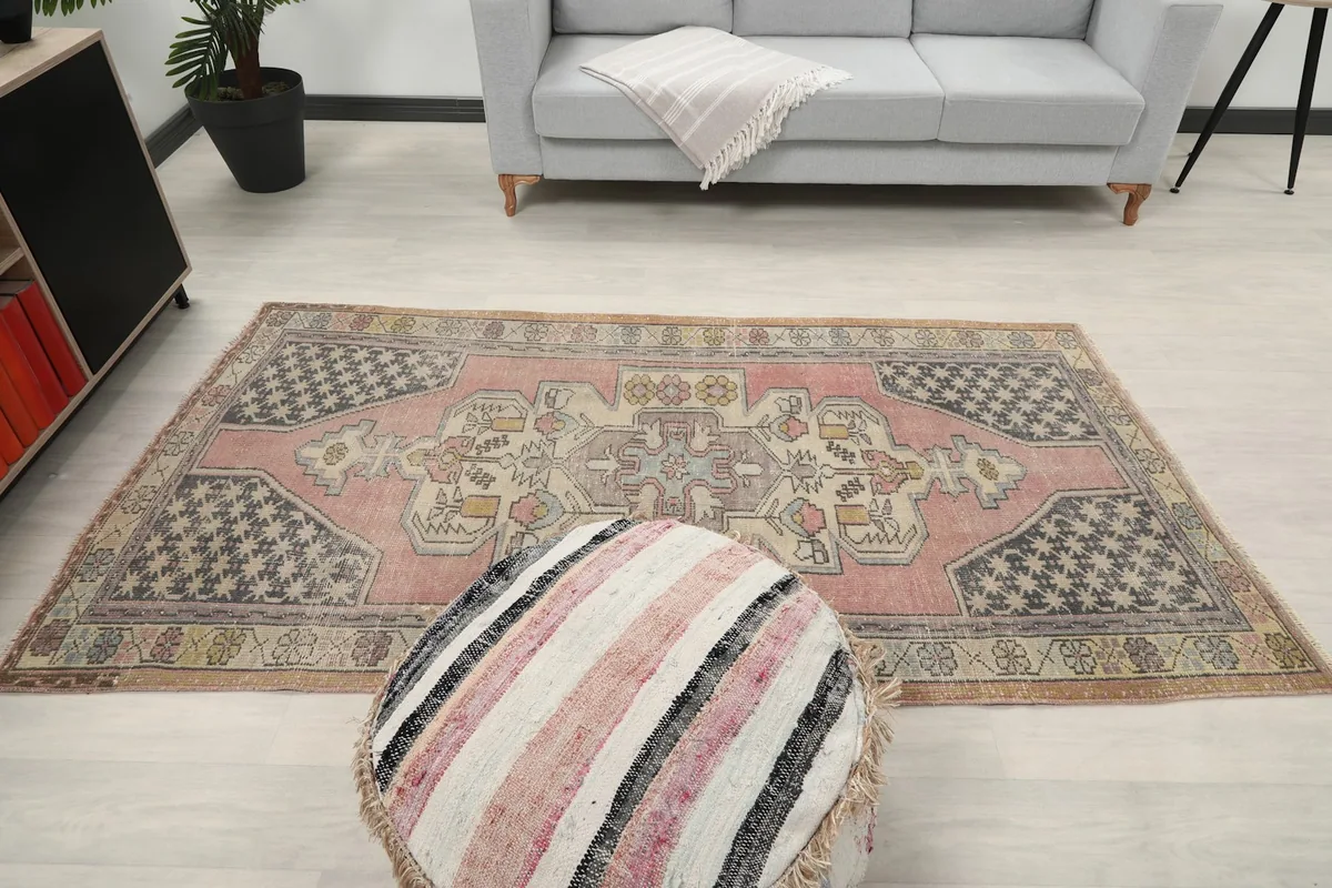 Top-down view of the rose rug in a room, with a striped pouf in the foreground