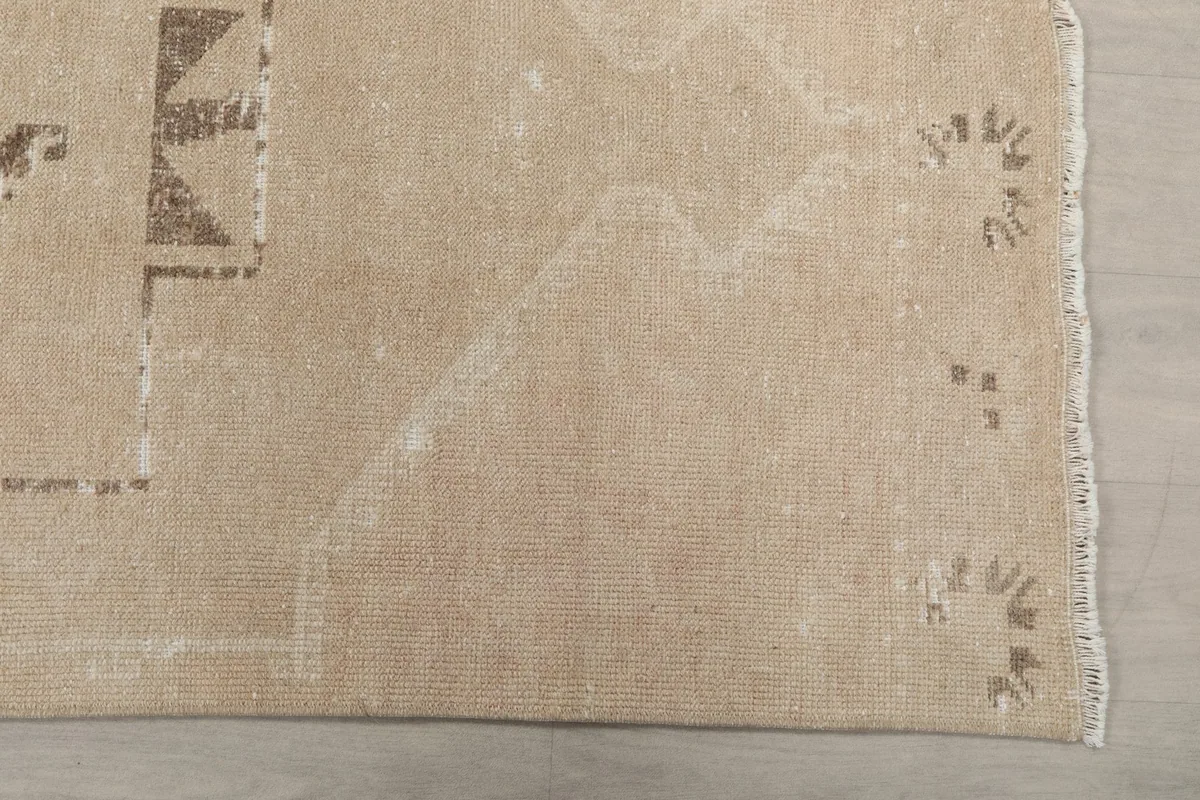 Close-up detail of the end of the beige runner rug, showing the fringe and subtle brown tribal patterns
