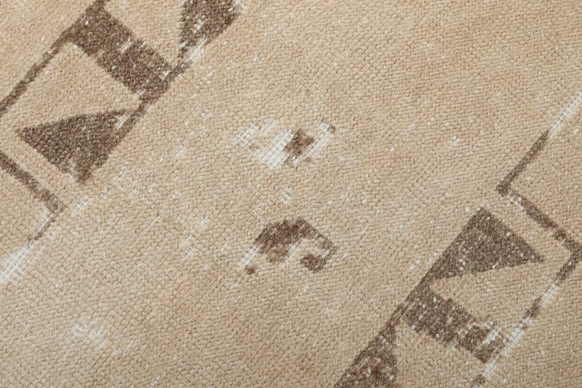 Close-up of the distressed texture and intricate brown tribal patterns within the beige field of the rug