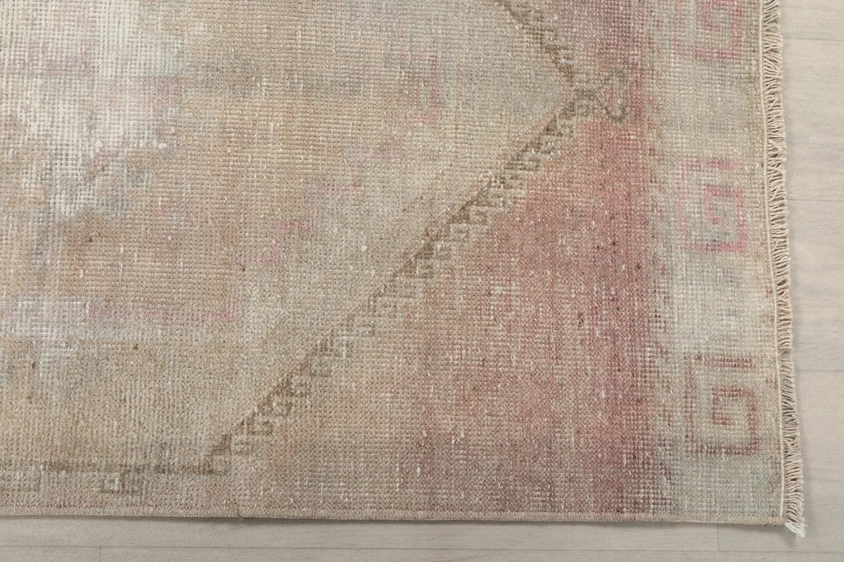 Detailed view of the rug's end, highlighting the subtle geometric border and faded rose hues