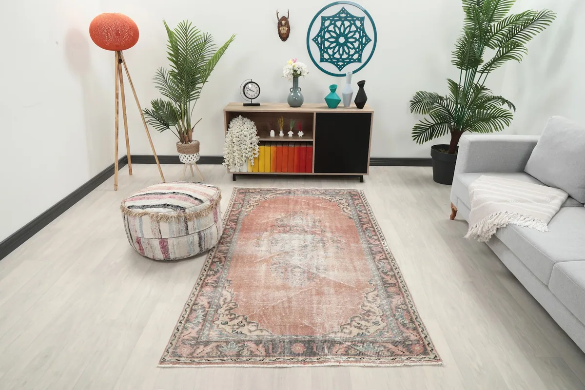 Vintage rose Anatolian rug displayed in a living room setting with a light couch and plants.