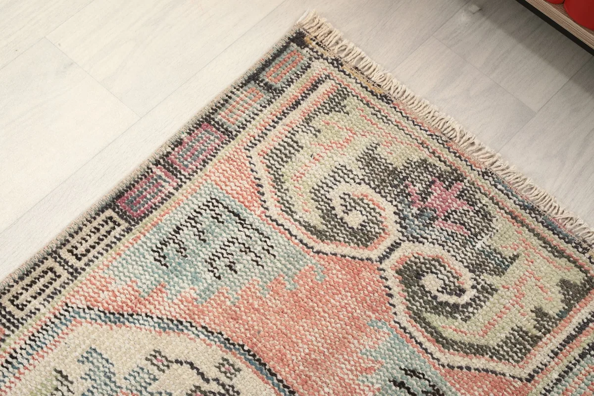 Detail of the rug's upper left corner, showing the geometric border pattern and fringe.