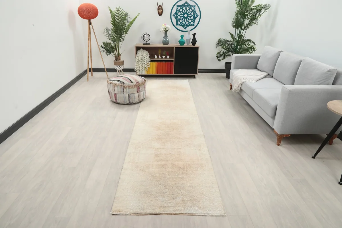 Long view of the beige runner rug in a modern living room setting with a sofa and ottoman.
