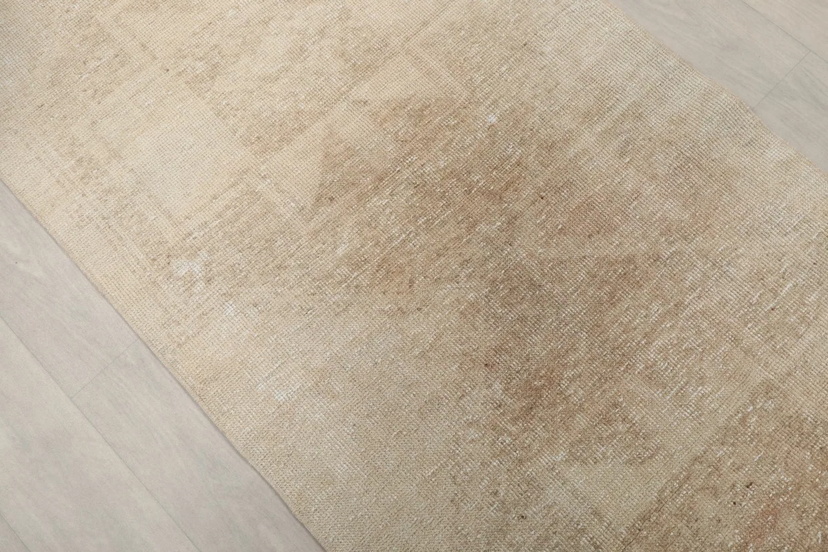 Angled close-up showing the faded geometric motifs and texture of the rug's beige field.