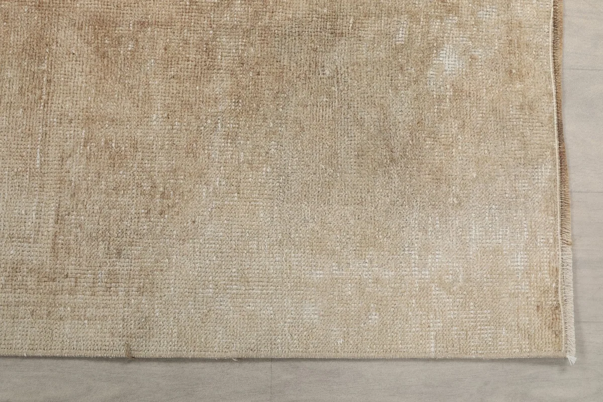 Detailed view of the low wool pile and distressed surface of the beige vintage rug.