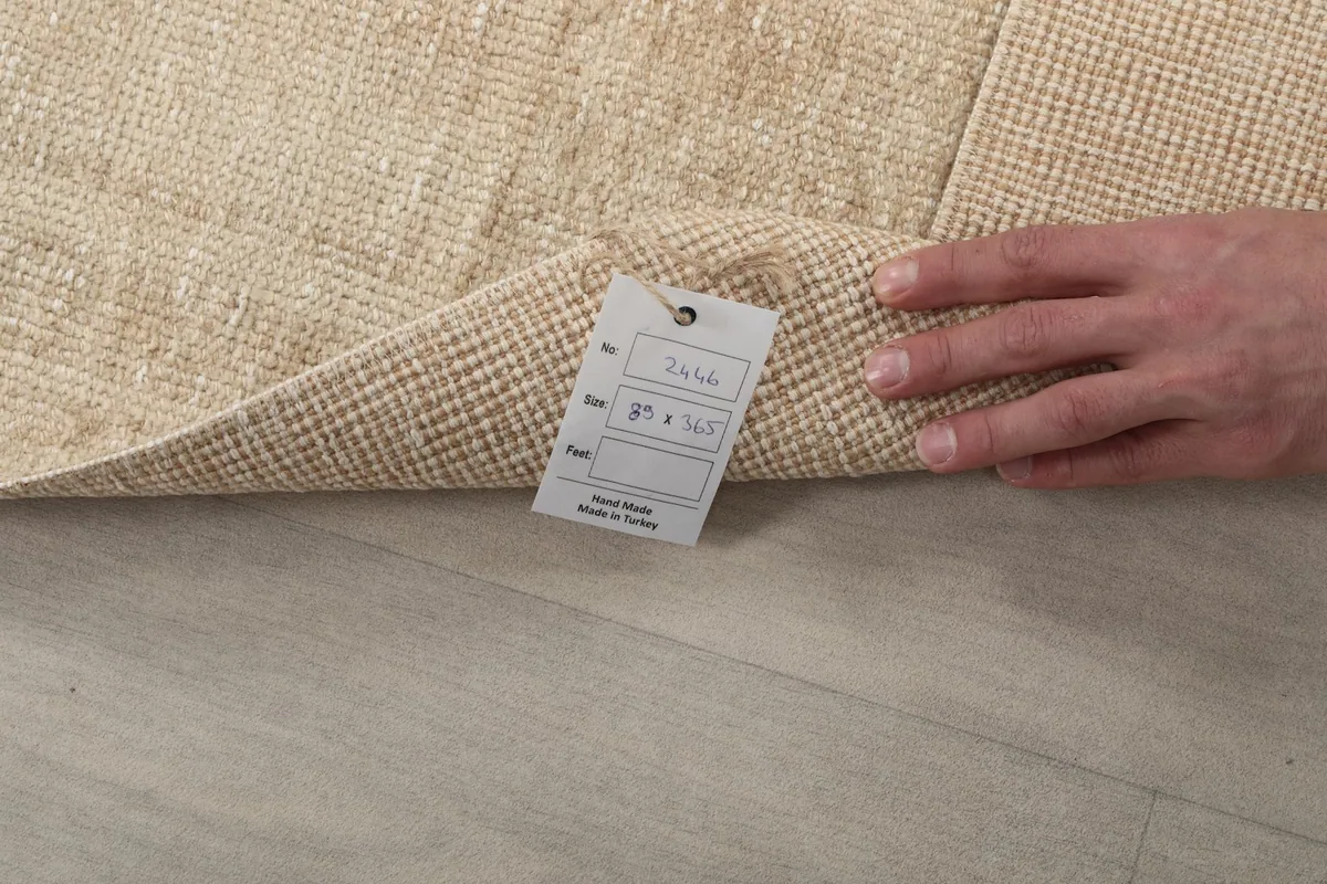 A hand holding a tag with rug details, showing the back of the hand-knotted vintage runner.