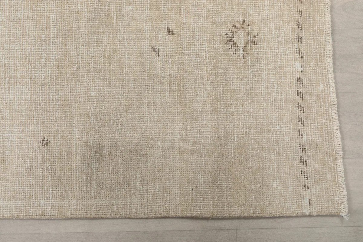 Detailed overhead view of the rug's beige field and faint brown geometric motifs near the edge.