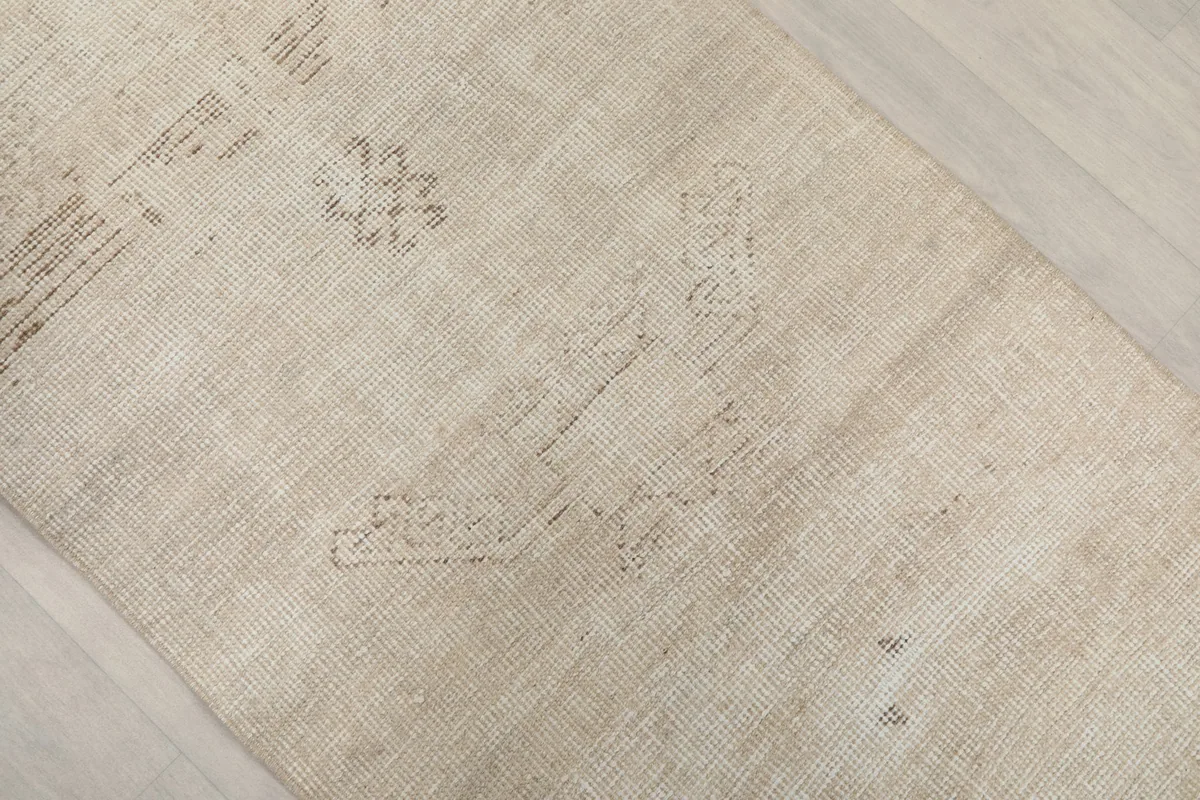 Close-up of the rug's surface, showing the subtle, worn geometric designs and natural variations in the beige color.