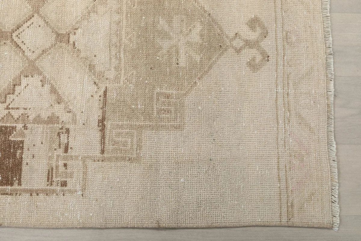 Detailed view of the ivory field and brown geometric motifs, showing the rug's texture and edge