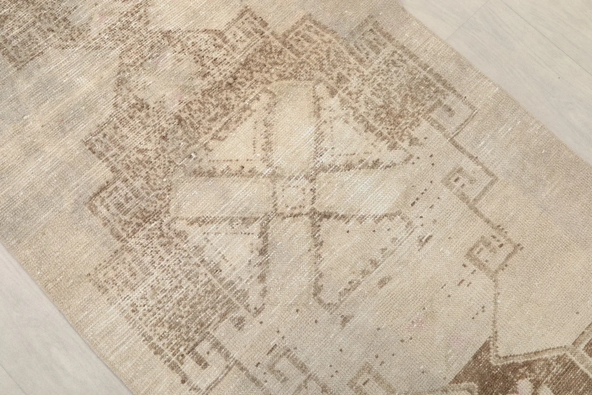 Close-up of a central geometric motif in brown on the ivory runner, highlighting the hand-knotted detail
