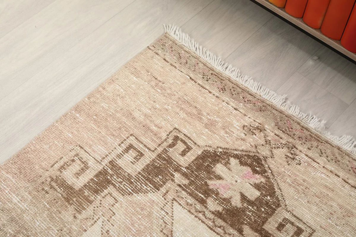 Detail of the rug's end and fringe, showing the intricate brown geometric pattern against the ivory