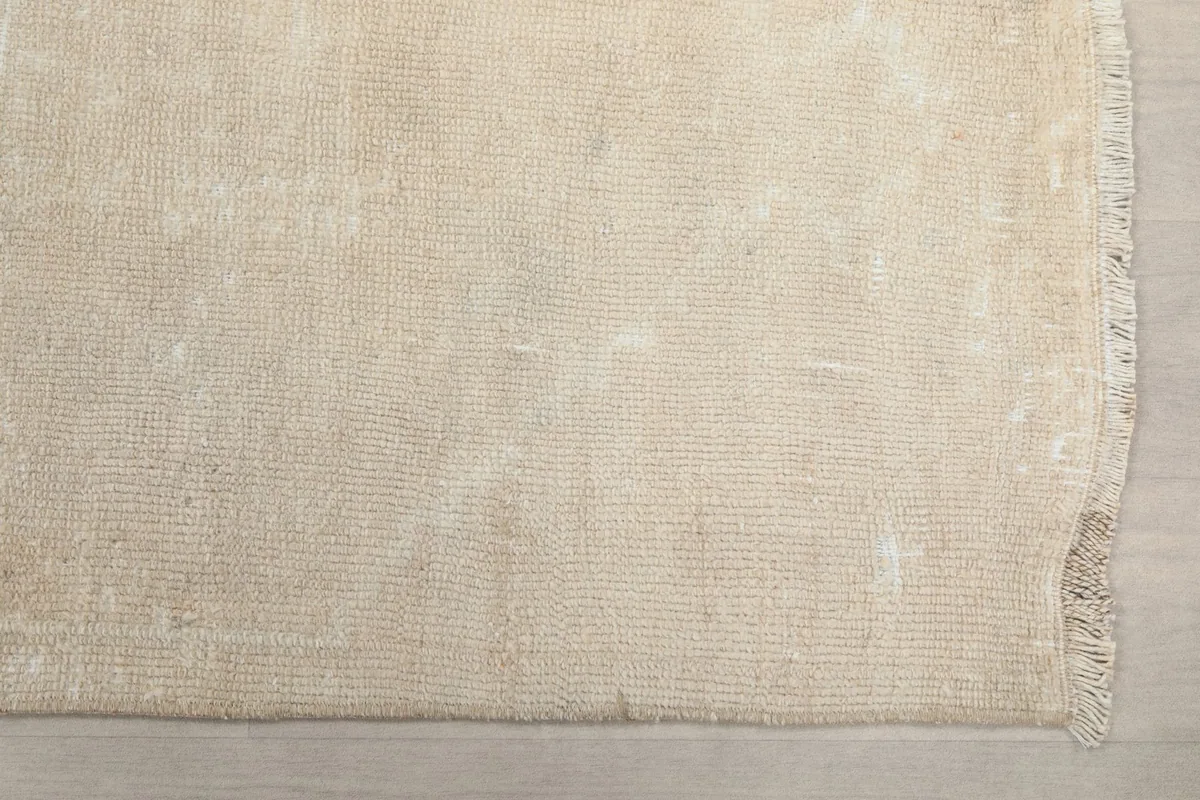 Detailed overhead view of the end of the beige runner rug, showing the distressed pile and edge.