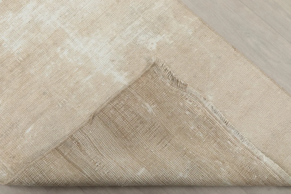 Corner of the rug folded back to show the cotton foundation and the reverse side of the hand-knotting.
