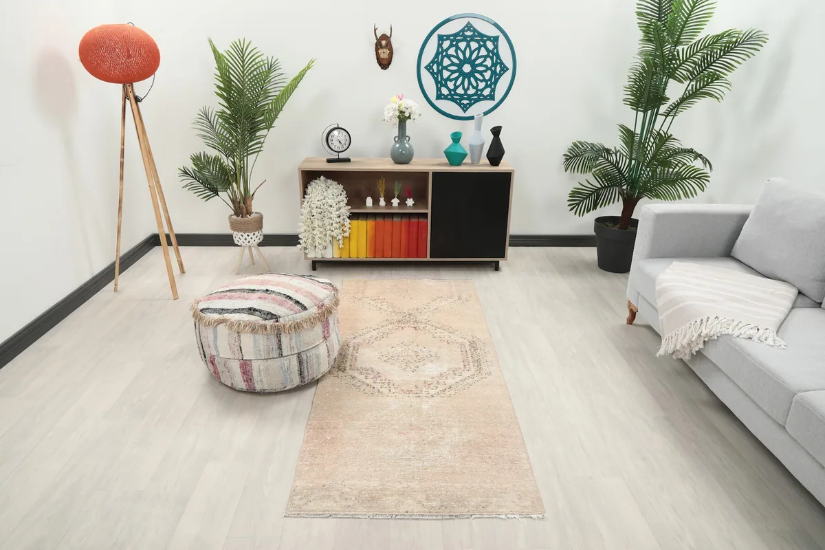 Beige and rose runner rug in a living room setting, showing its scale next to a sofa and ottoman.