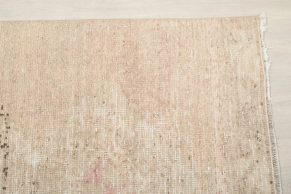 Detail of the rug's surface, showing the subtle rose and beige tones and low pile texture.