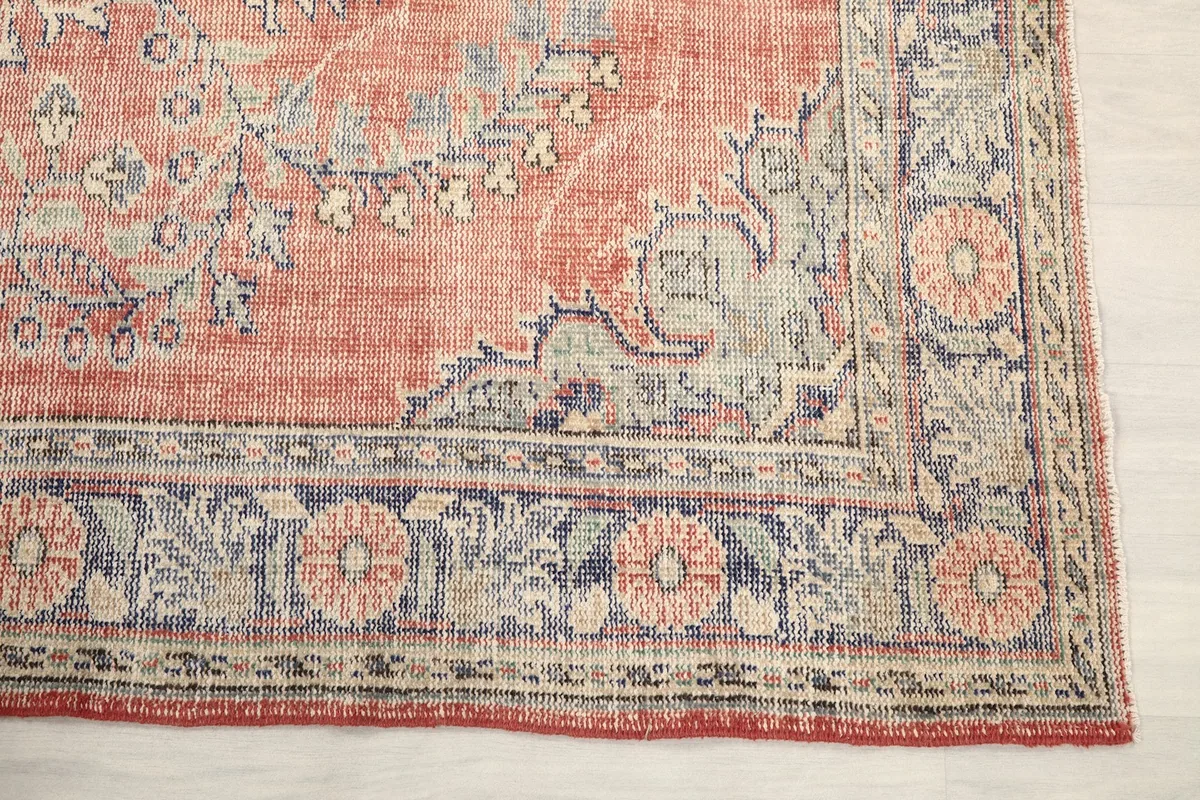 Close-up of the rug's corner, showing the floral border and faded rust tones
