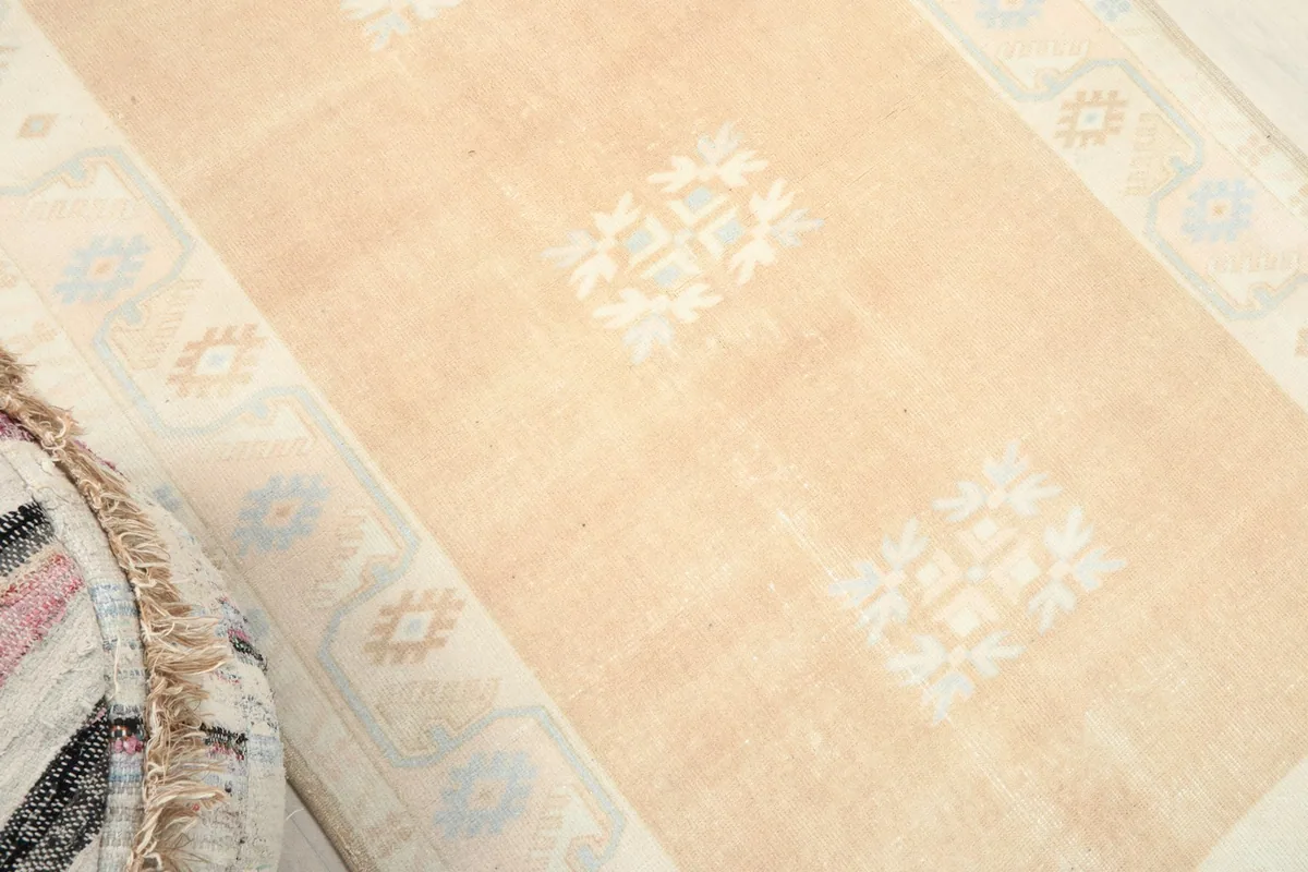 Angled view of the tan rug's center and border, highlighting the subtle geometric patterns