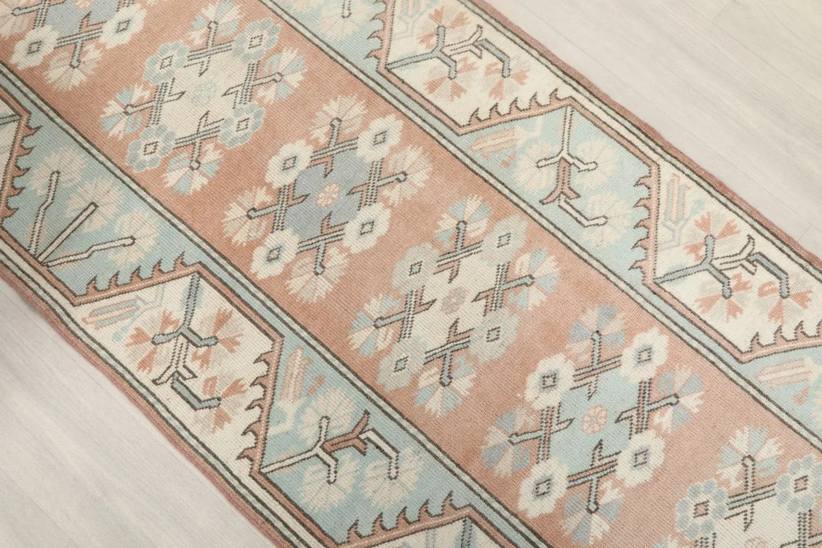 Angled view of the runner rug's central peach field and blue borders with intricate patterns