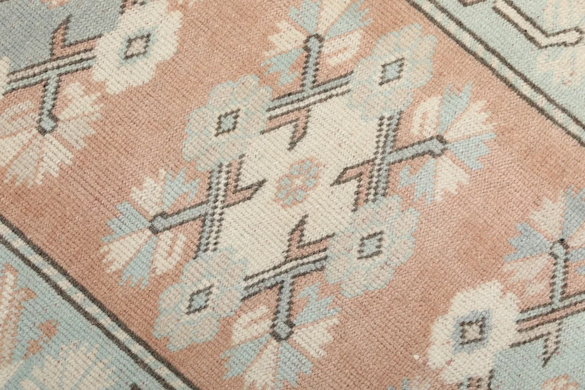Close-up detail of the hand-knotted pile, showing the peach, blue, and ivory geometric motifs