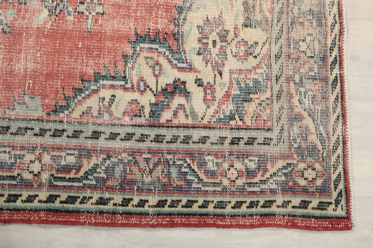 Detailed view of the rug's border pattern, featuring blue, beige, and rose tones