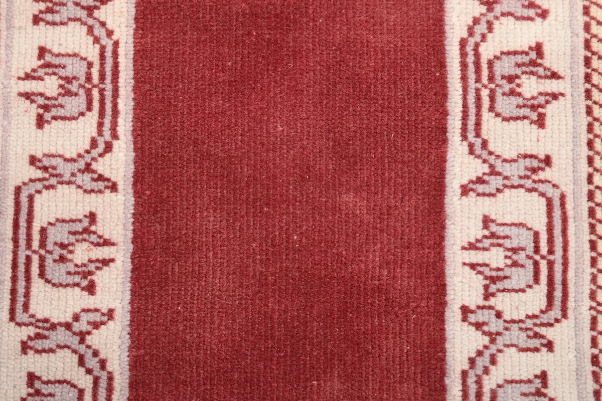 Close-up of the rug's central red field and a section of the cream border with floral-like motifs.