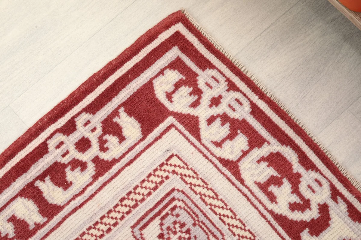 Detailed shot of the rug's corner, focusing on the intricate cream border design against the red.