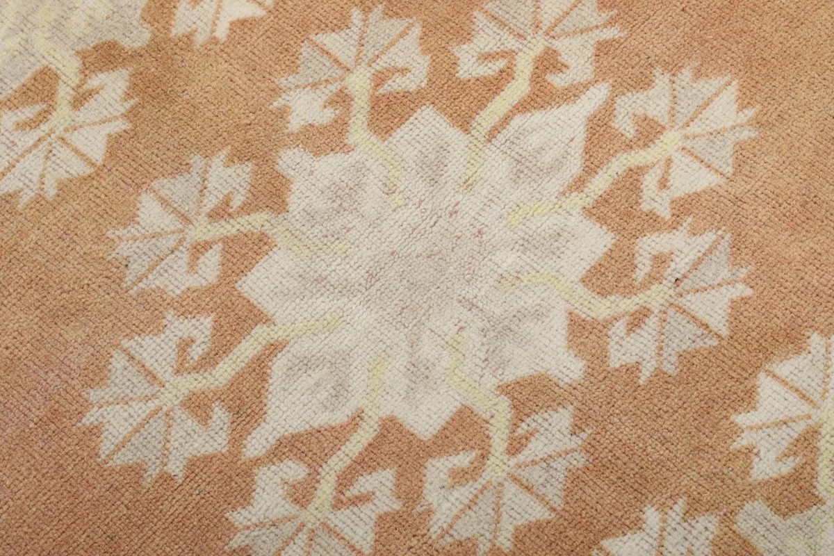 Macro detail of a cream floral motif within the orange field, showing the hand-knotted texture.