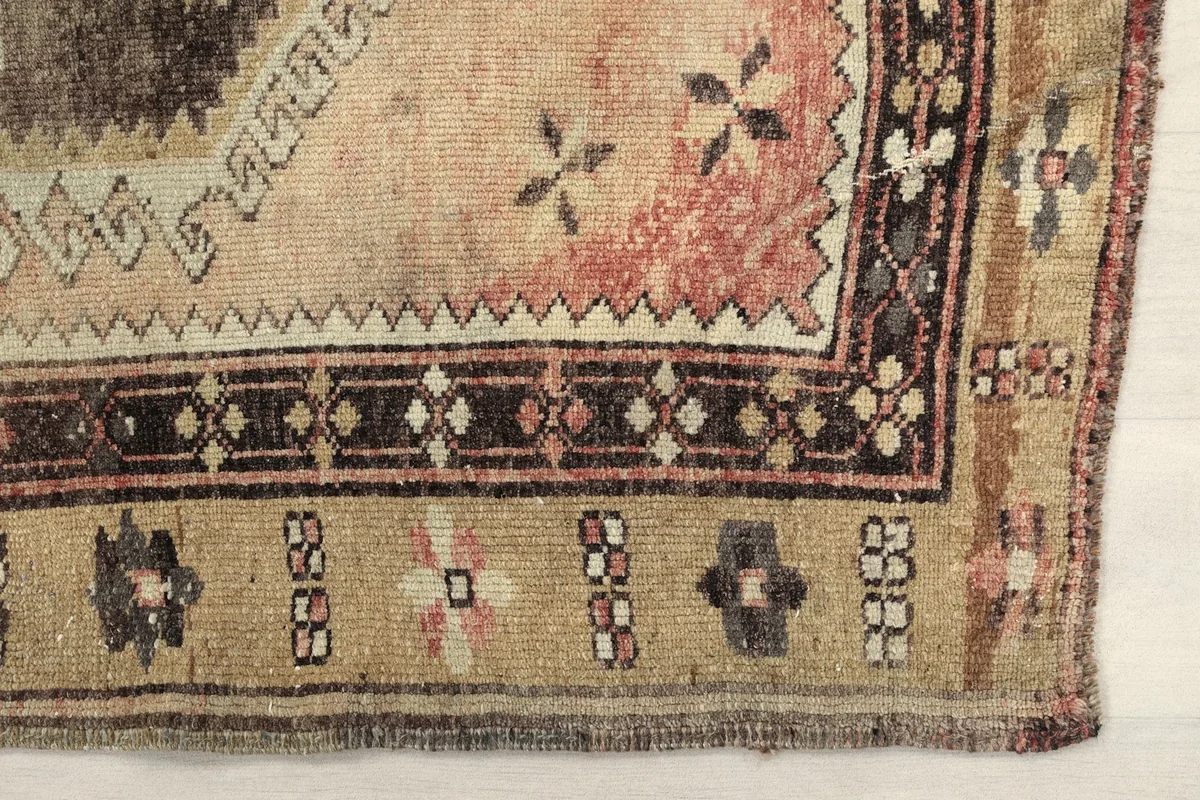 Detailed view of the rug's corner with tan border, showing geometric patterns and subtle color variations