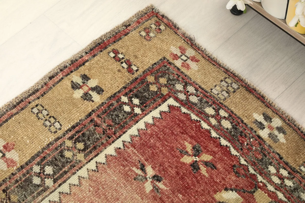 Close-up of the rug's border design, revealing intricate tan, charcoal, and rose patterns