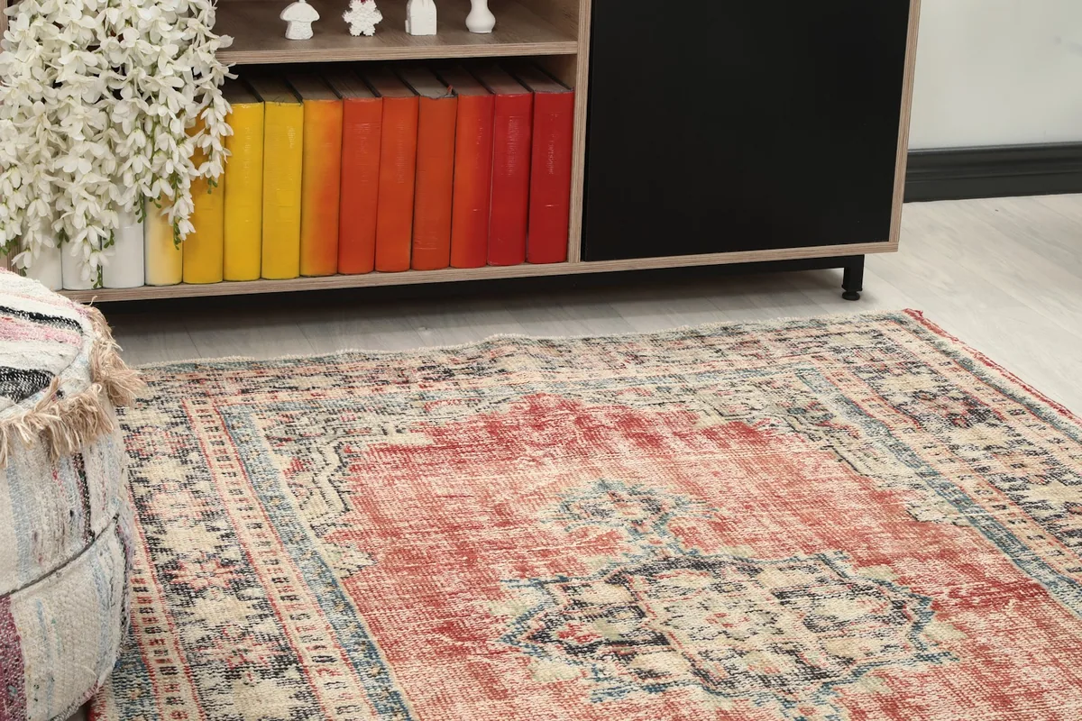 Close-up of the rug's rose field and border, showing subtle color variations and patina next to furniture