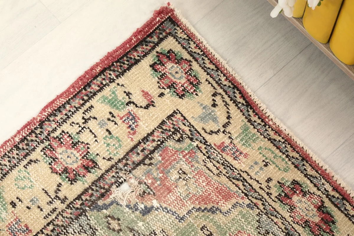 Corner detail of the rug, showing the blend of rose, beige, green, and blue hues in the motifs