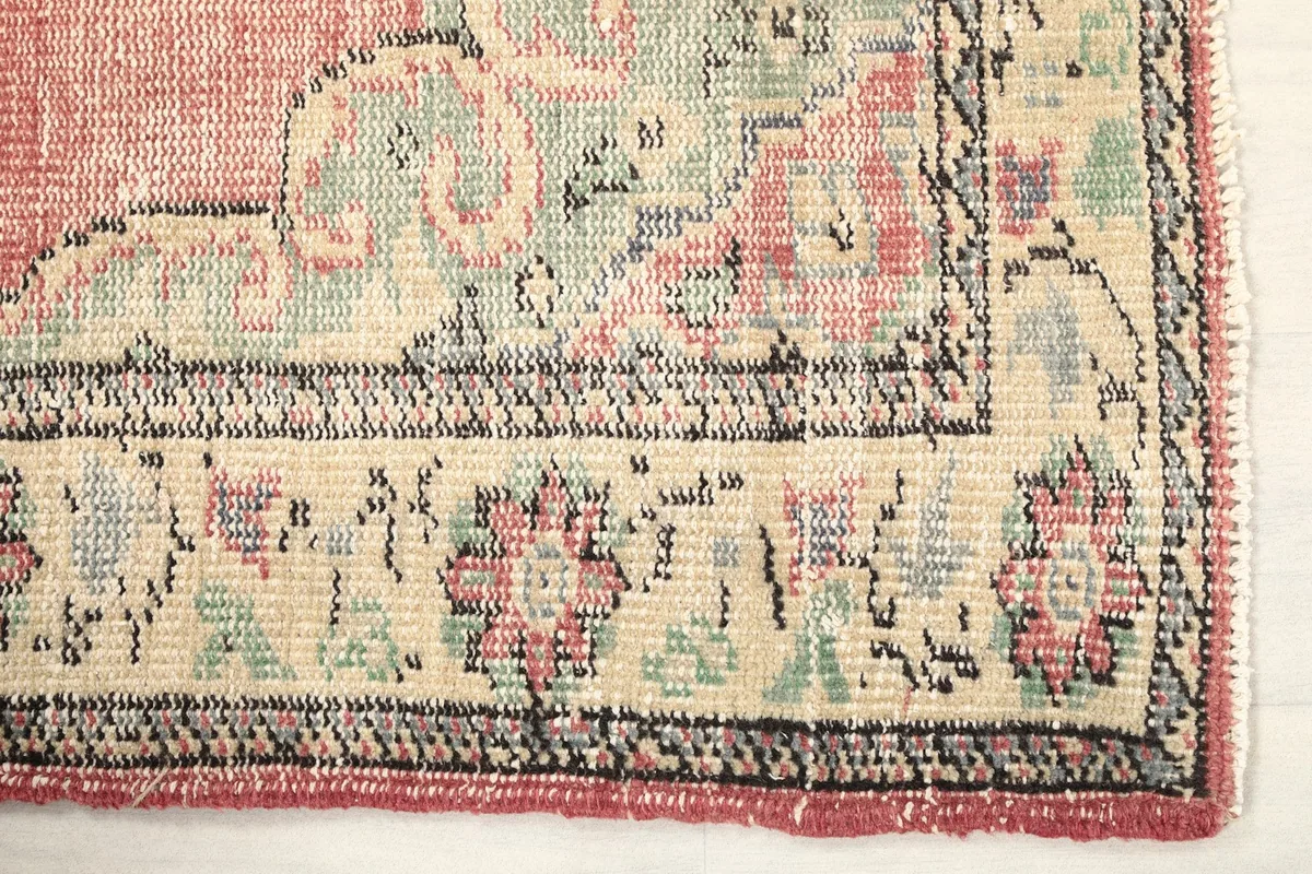 Detailed view of the rug's border design, featuring floral and geometric patterns in beige, rose, and green